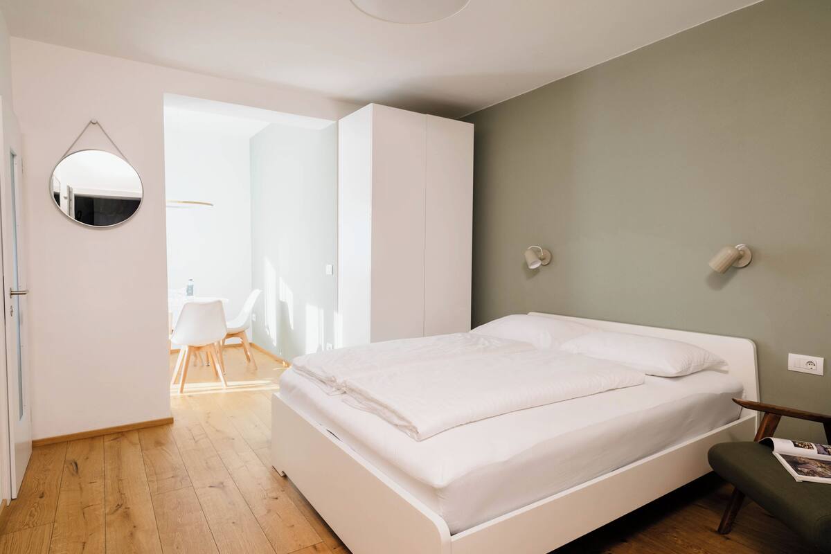 A bedroom with a bed, a bedside table, a chair, a mirror, and a wardrobe.