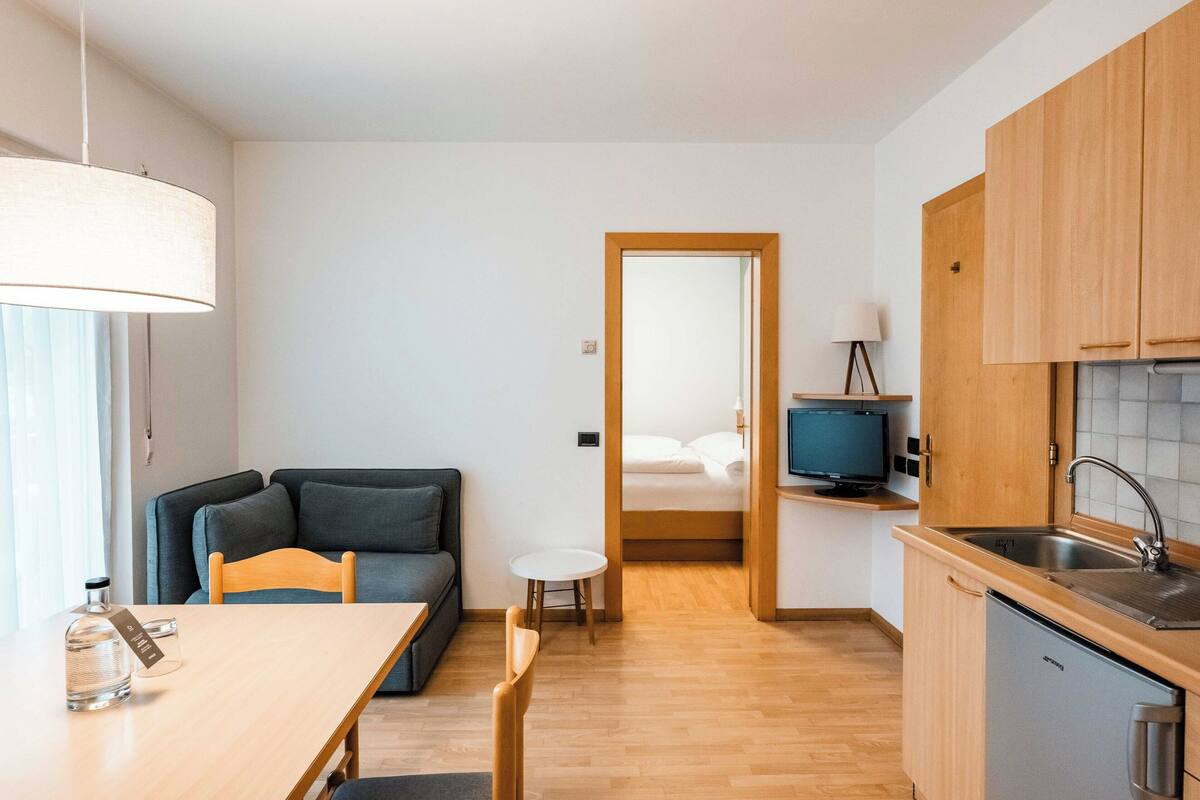 A modern, compact living space with a kitchenette, a dining area, and a bedroom visible through an open door.