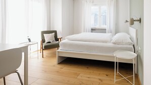 Un dormitorio moderno con cama, una silla, una mesita y una ventana con cortinas.