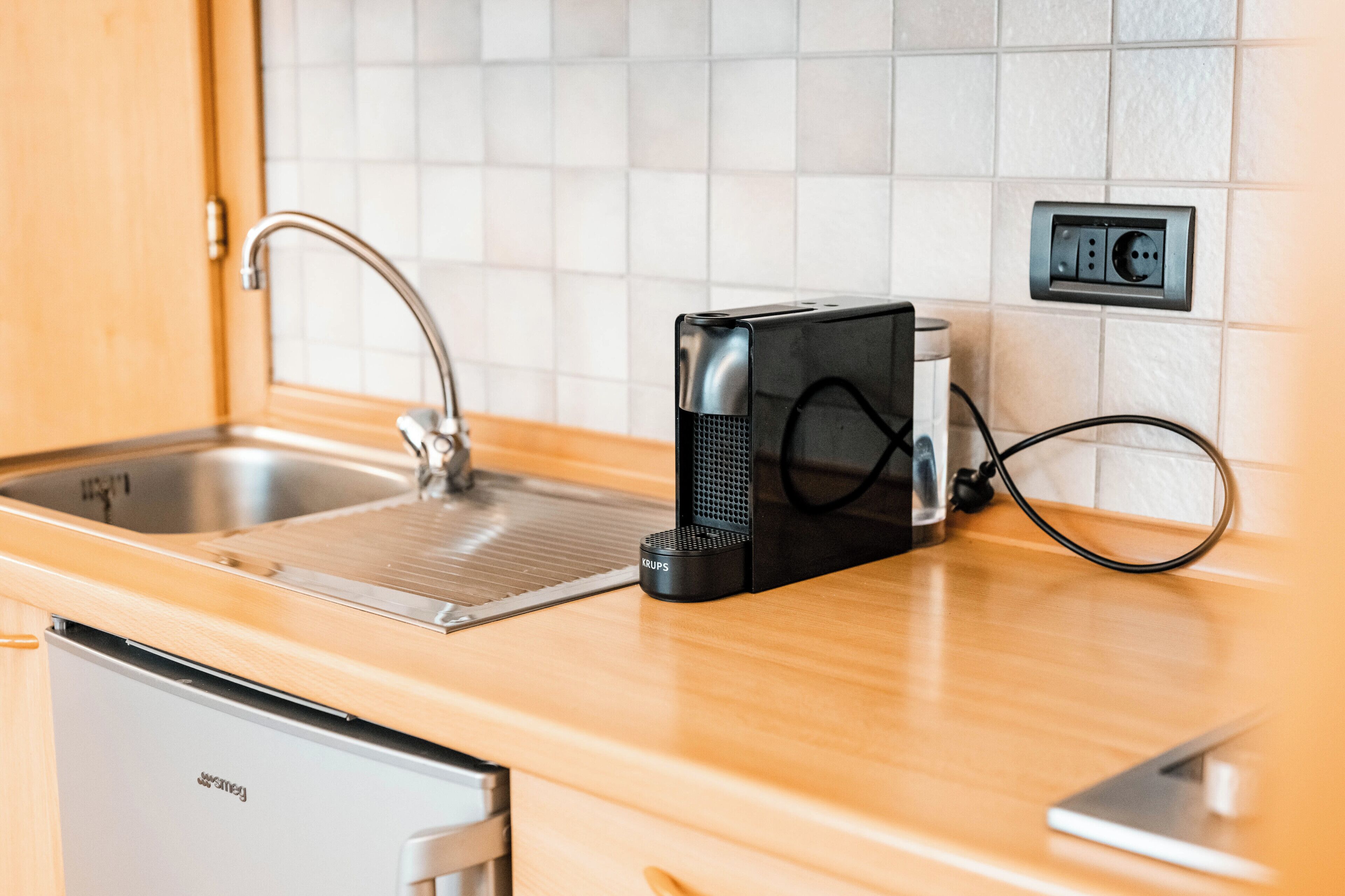 Una cocina con lavavajillas integrado, cafetera, fregadero y un enchufe en la pared.