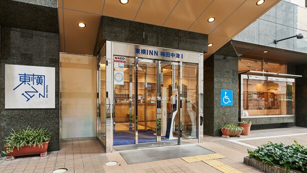 La entrada de un edificio con puertas de vidrio, un letrero con caracteres japoneses y el símbolo de accesibilidad para sillas de ruedas.