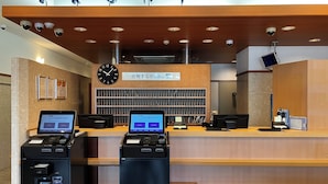 Zona de recepción de un hotel con un mostrador de madera, dos pantallas digitales, un reloj y un letrero que indica la recepción.