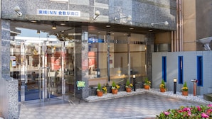 Entrada de hotel con puertas de vidrio, un cartel que indica el camino a la recepción y plantas en macetas en el área de entrada.