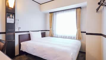 Une chambre d’hôtel comprenant un lit, un bureau, une chaise, une fenêtre avec des rideaux et un luminaire fixé au mur.