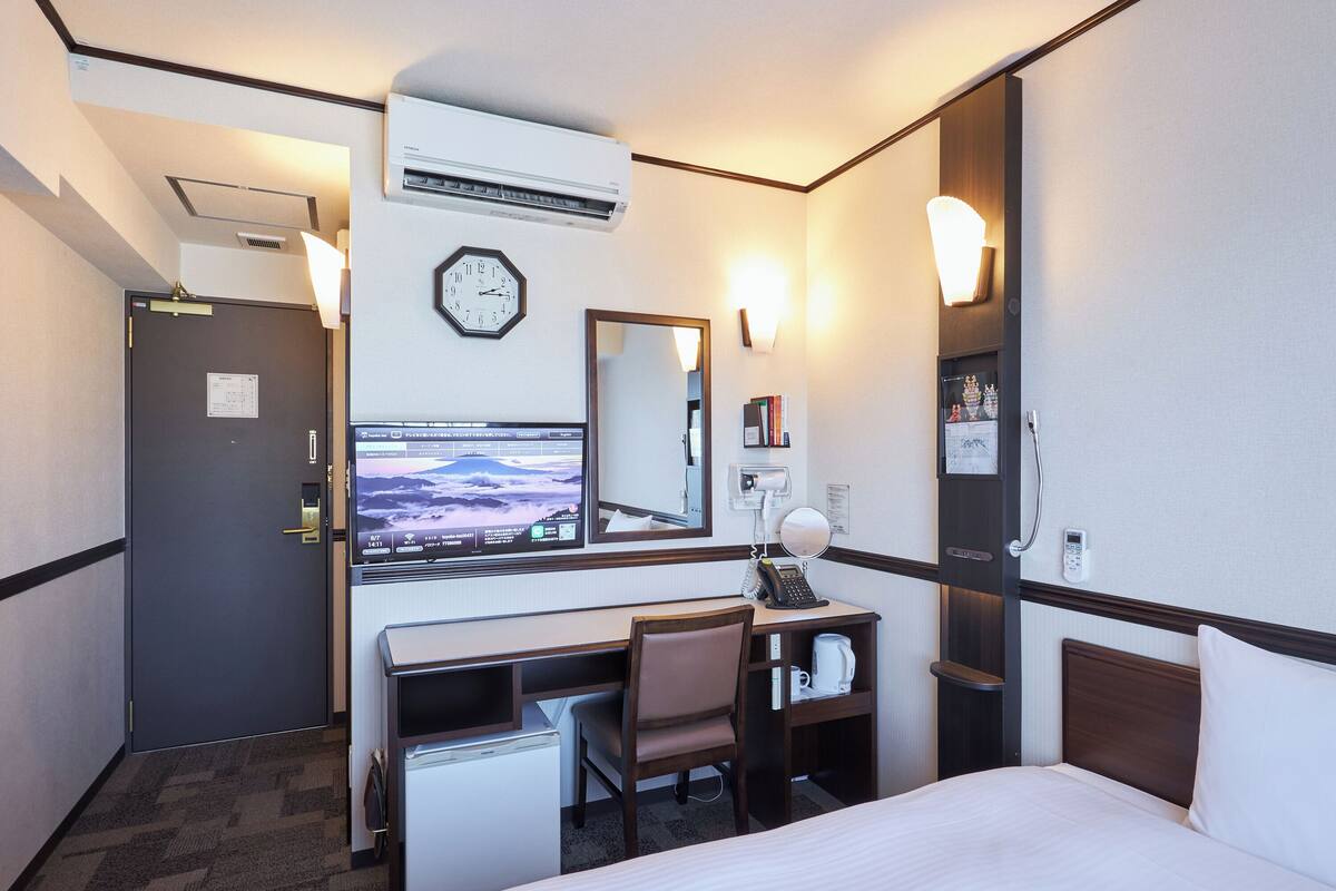 A hotel room with a bed, desk, chair, and a TV displaying a mountain view.