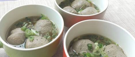 Three bowls of soup with meatballs and green onions on a table.