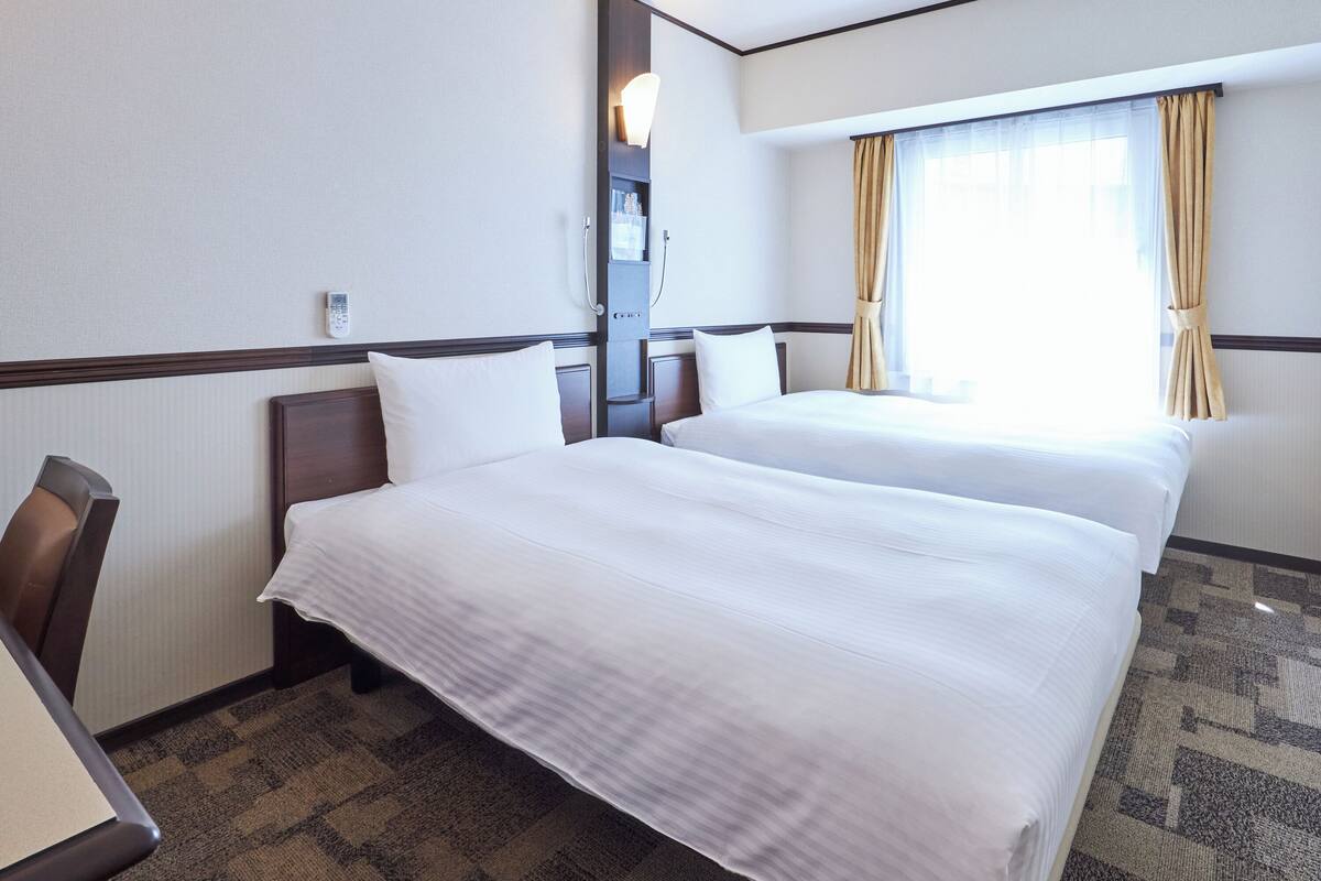 A hotel room with two beds, a desk, and a window with curtains.