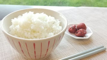 A bowl of white rice with chopsticks and a small plate of red items on a table.