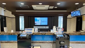 A hotel reception area with a digital screen displaying a welcome message, a cash register, and a small desk with a computer monitor. - Toyoko Inn Osaka Semba Higashi (Osaka)