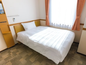 Een keurig opgemaakt bed met witte lakens, een houten hoofdbord en een klein nachtkastje met een lamp.