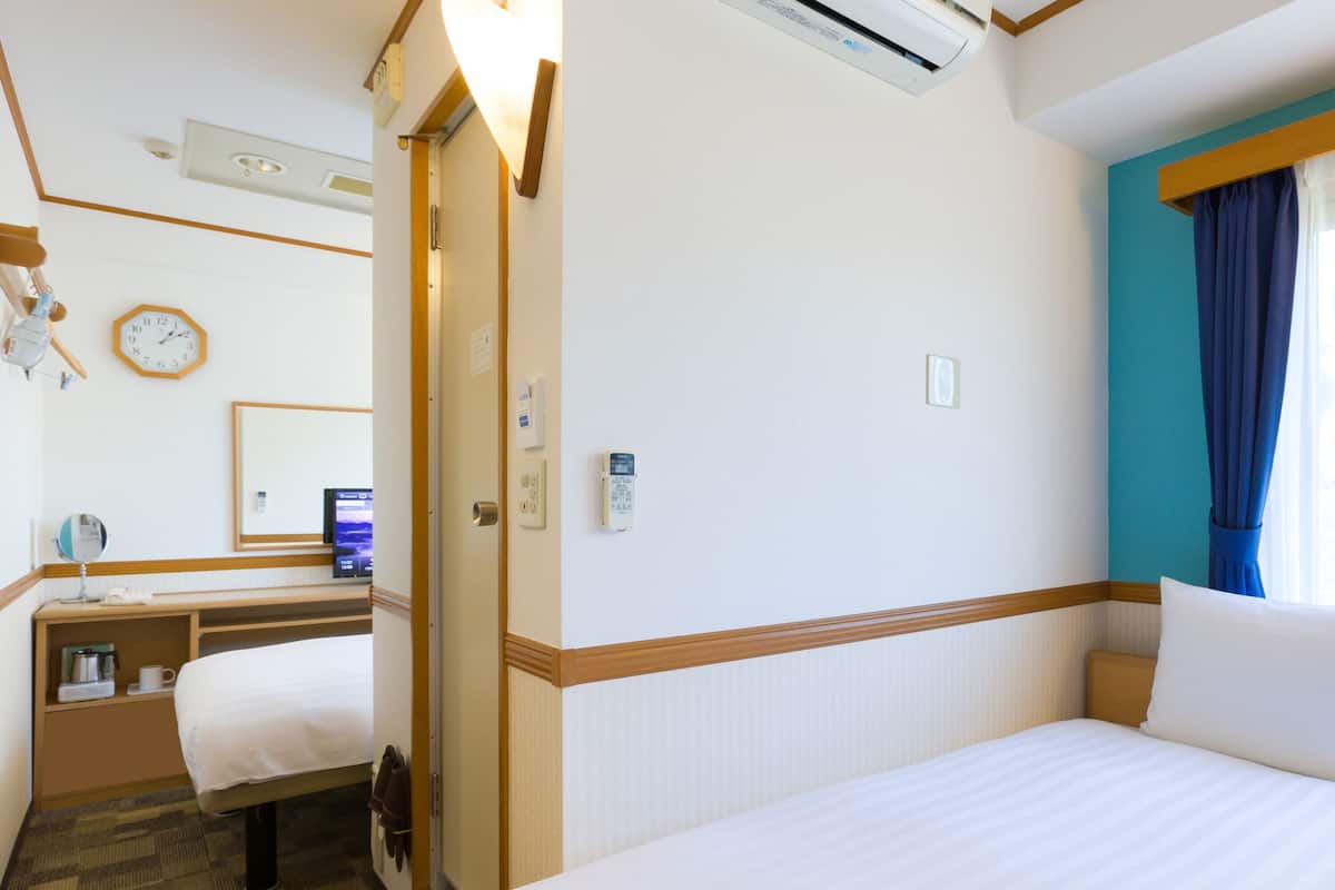 Una habitación de hotel con cama, escritorio, silla, reloj y ventana con cortinas.