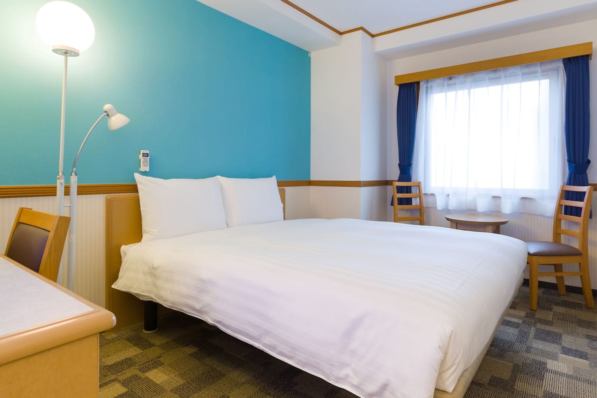 Una habitación de hotel con una cama grande, un escritorio, una silla, una lámpara y una ventana con cortinas.