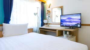 Hotelkamer met een bed, een bureau met een computer, een klok en een raam met gordijnen.