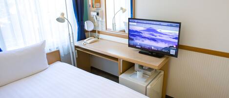 A hotel room with a bed, desk, and a television displaying a mountain scene.