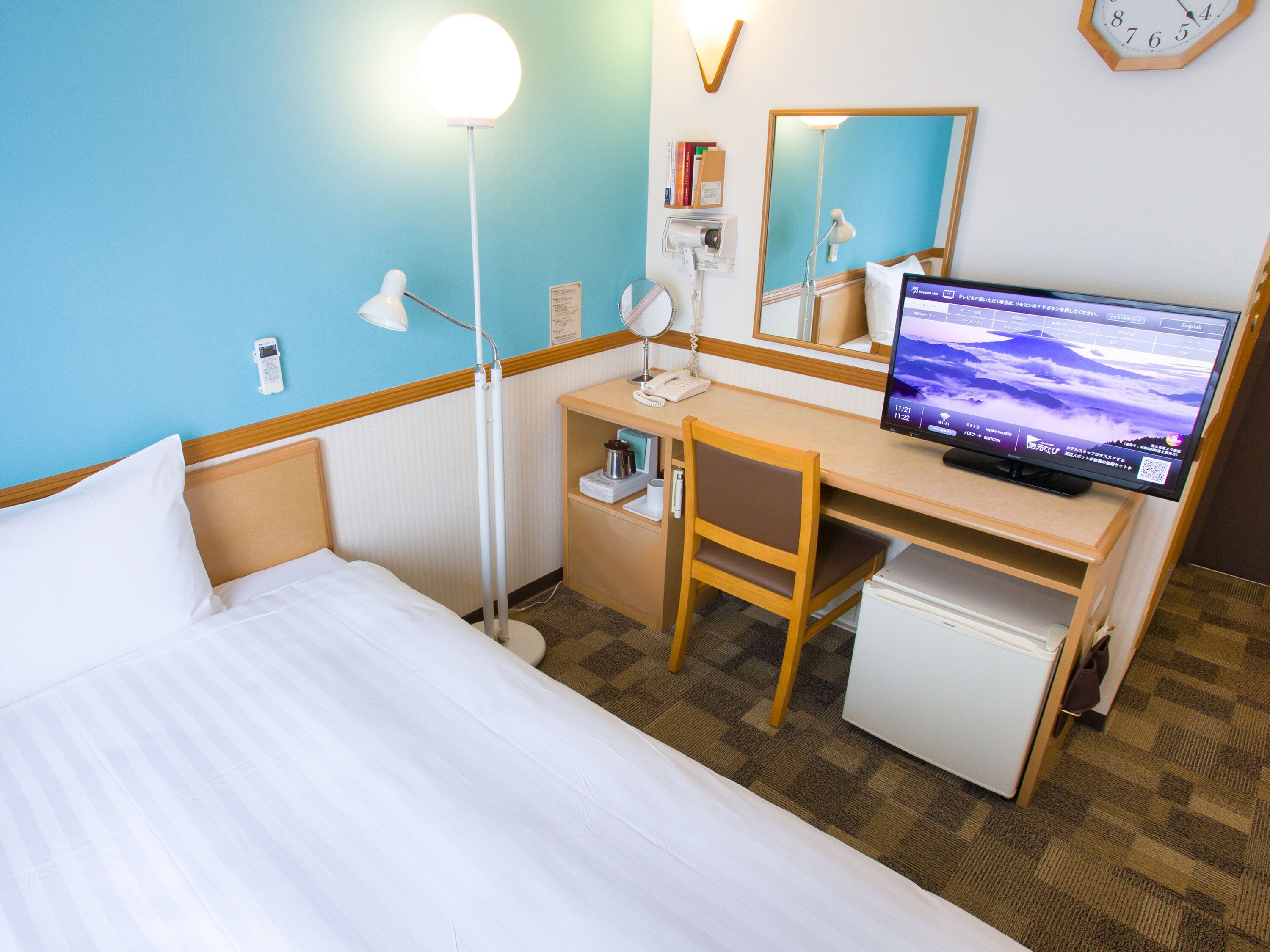 A hotel room with a bed, desk, chair, and a small refrigerator.