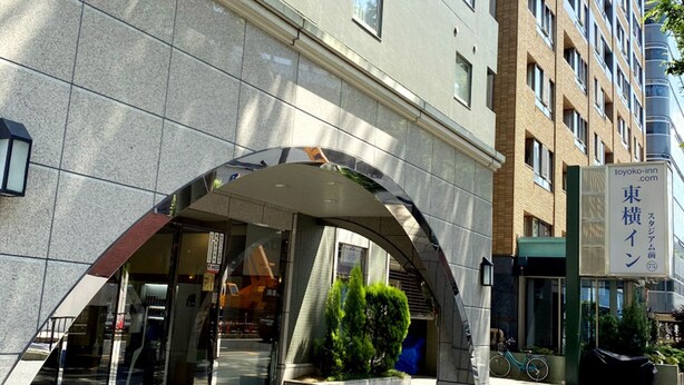 Een moderne hotelentree met een glazen gevel, een overdekte ingang en een bord met de naam "Toyoko Inn".