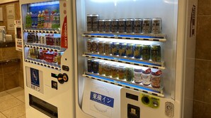 Automatische verkoopapparaten gevuld met drankjes en snacks, waaronder blikjes en flessen, in een zakelijke omgeving.