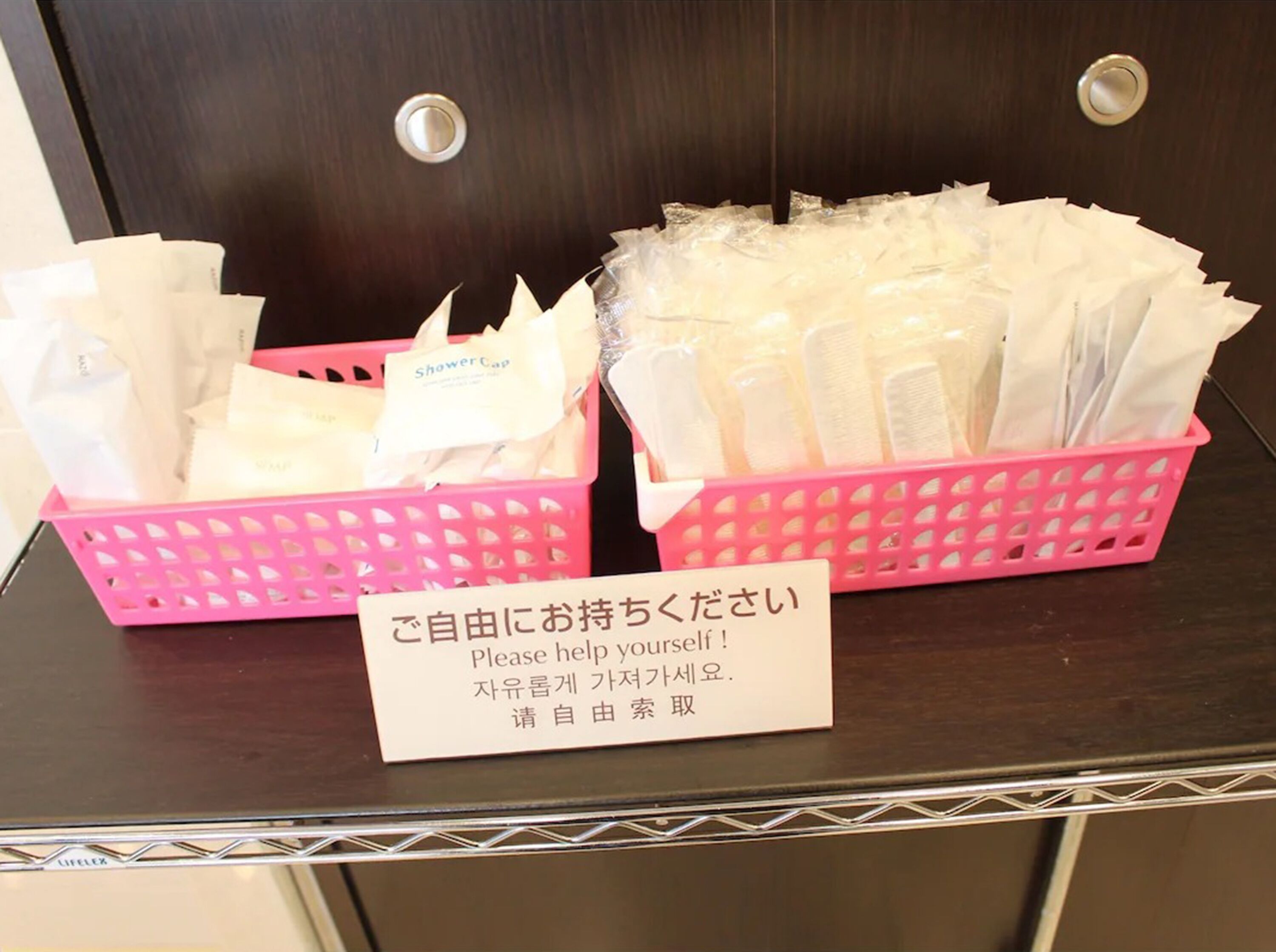 Two pink baskets filled with white towels and a sign in front of them.