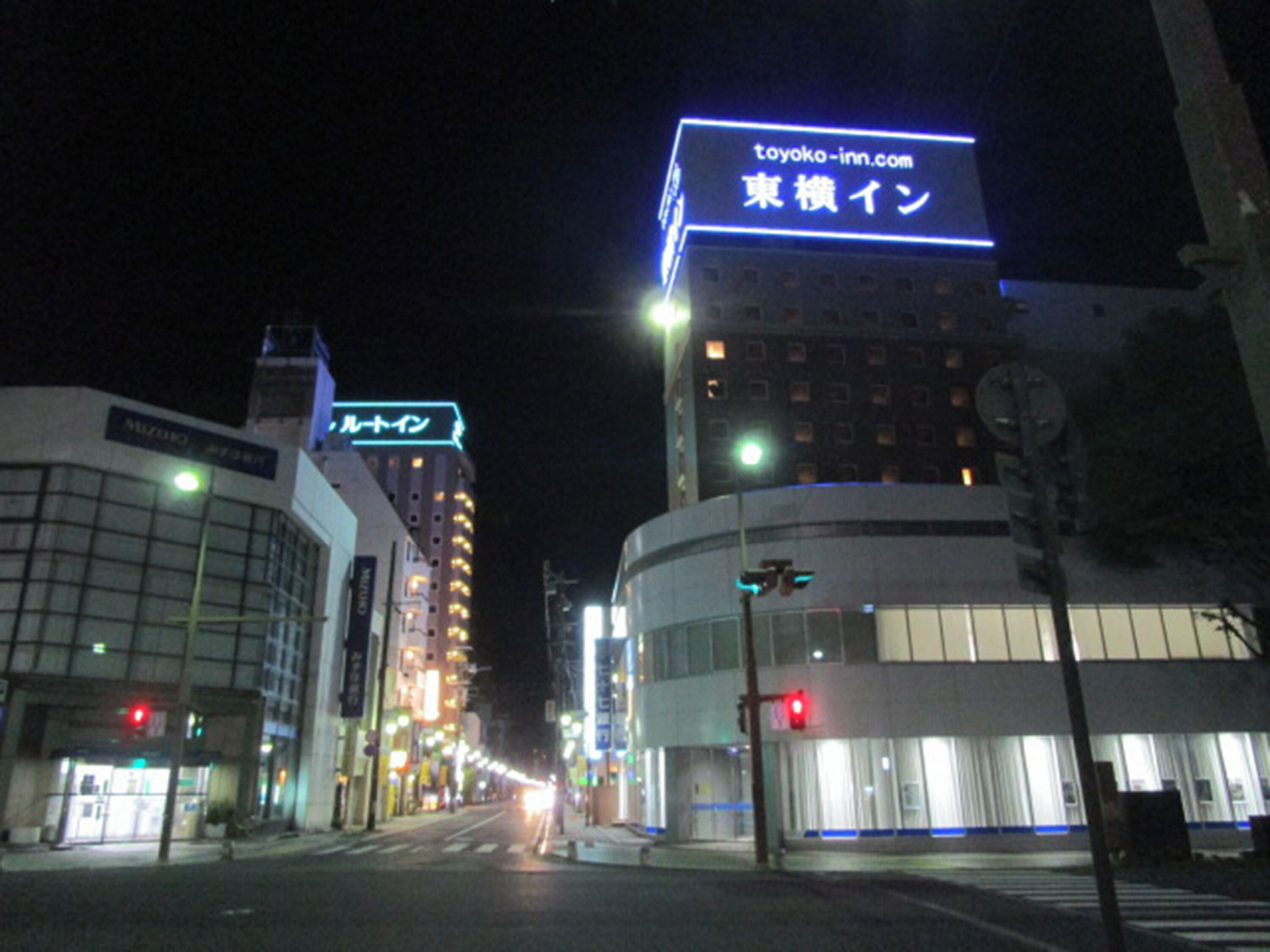 Une vue nocturne d’une ville, avec des enseignes lumineuses de l’hôtel Toyoko Inn et d’un autre hôtel.