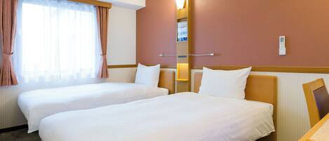 A hotel room with two beds, a large window with curtains, a wall-mounted light, and a small desk.