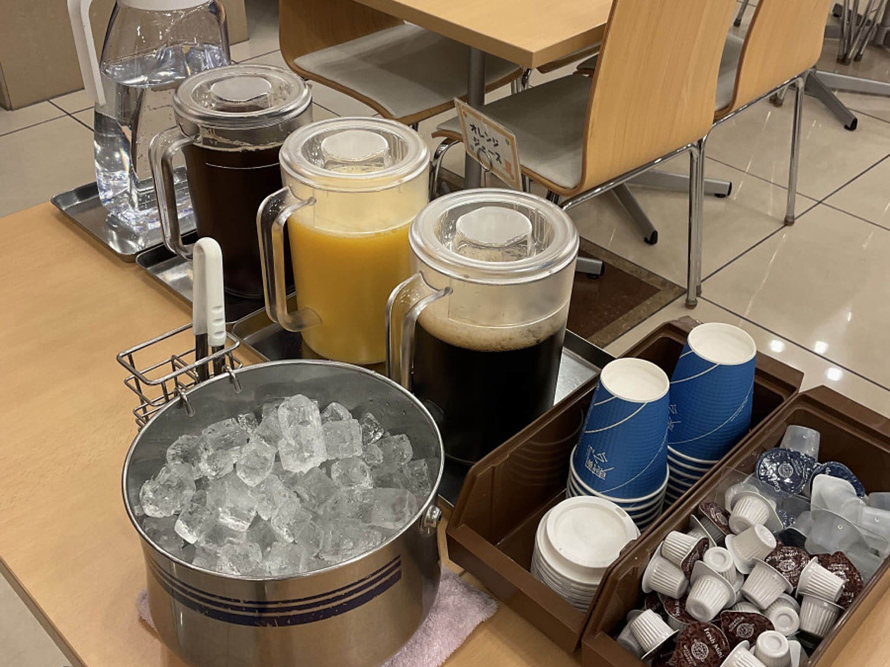 A beverage station with various drinks, ice, and disposable cups.