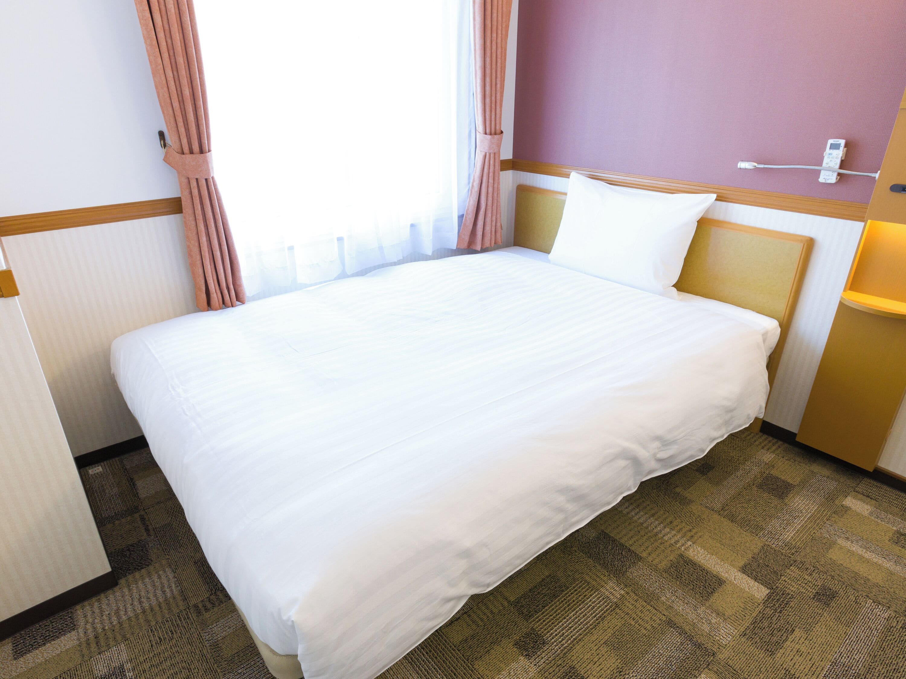 Una camera d'albergo con un letto grande, un comodino, una lampada e una finestra con tende.