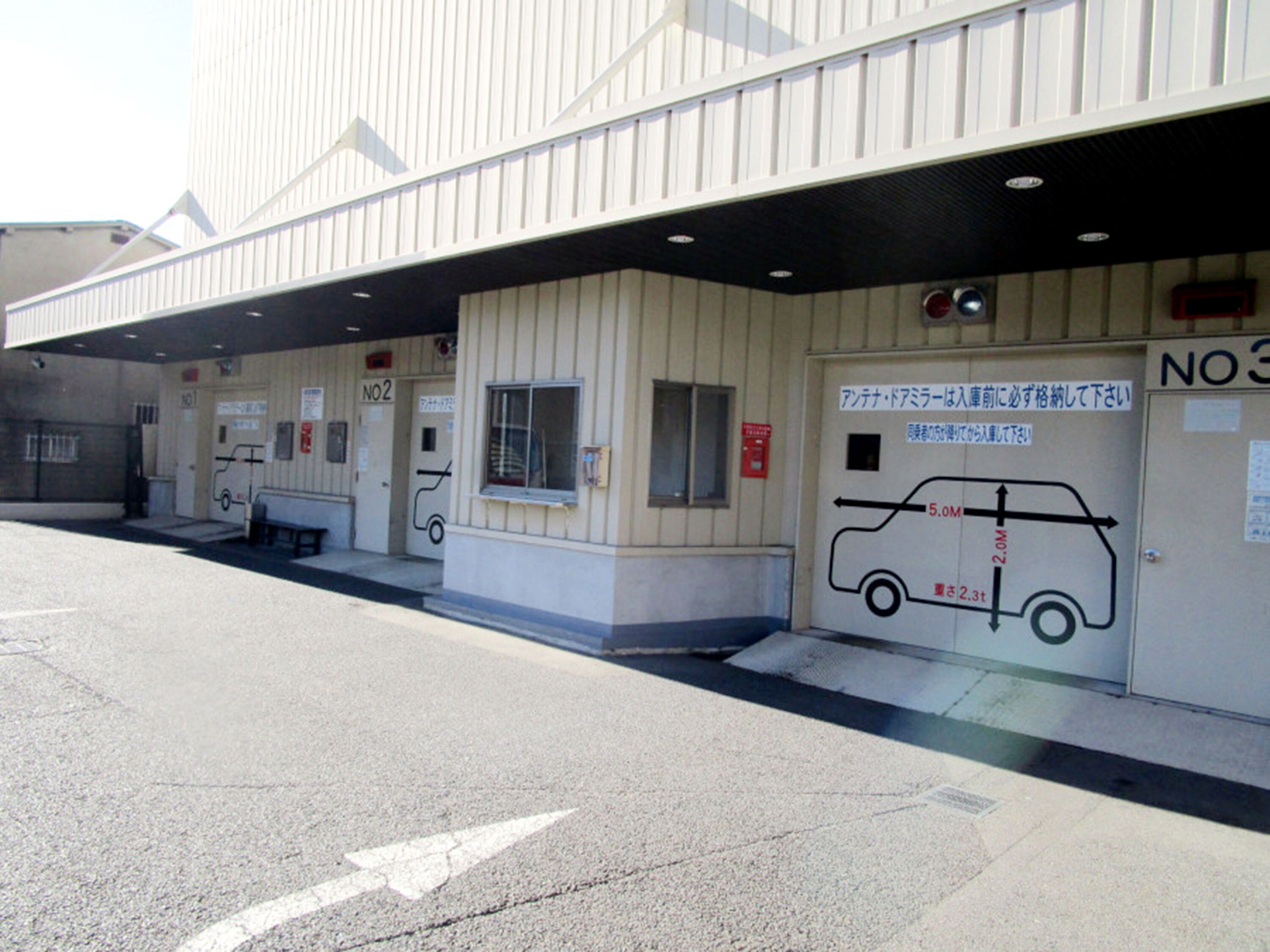 A building with a covered entrance, a sign indicating a height restriction of 2.3 meters, and a vehicle height limit of 5.0 meters.