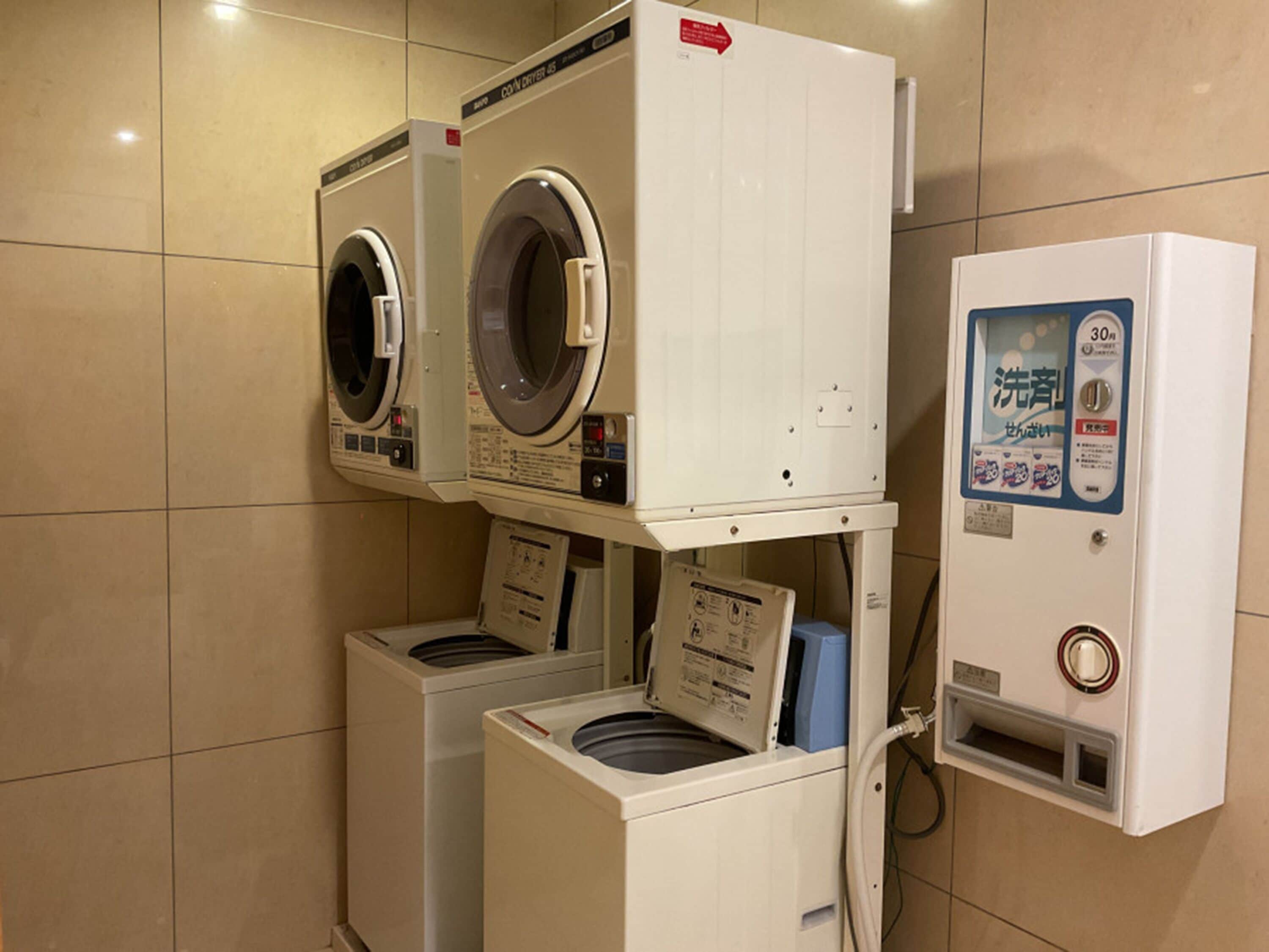 A laundry facility with two front-loading washing machines and a dryer, a control panel, and a water dispenser.