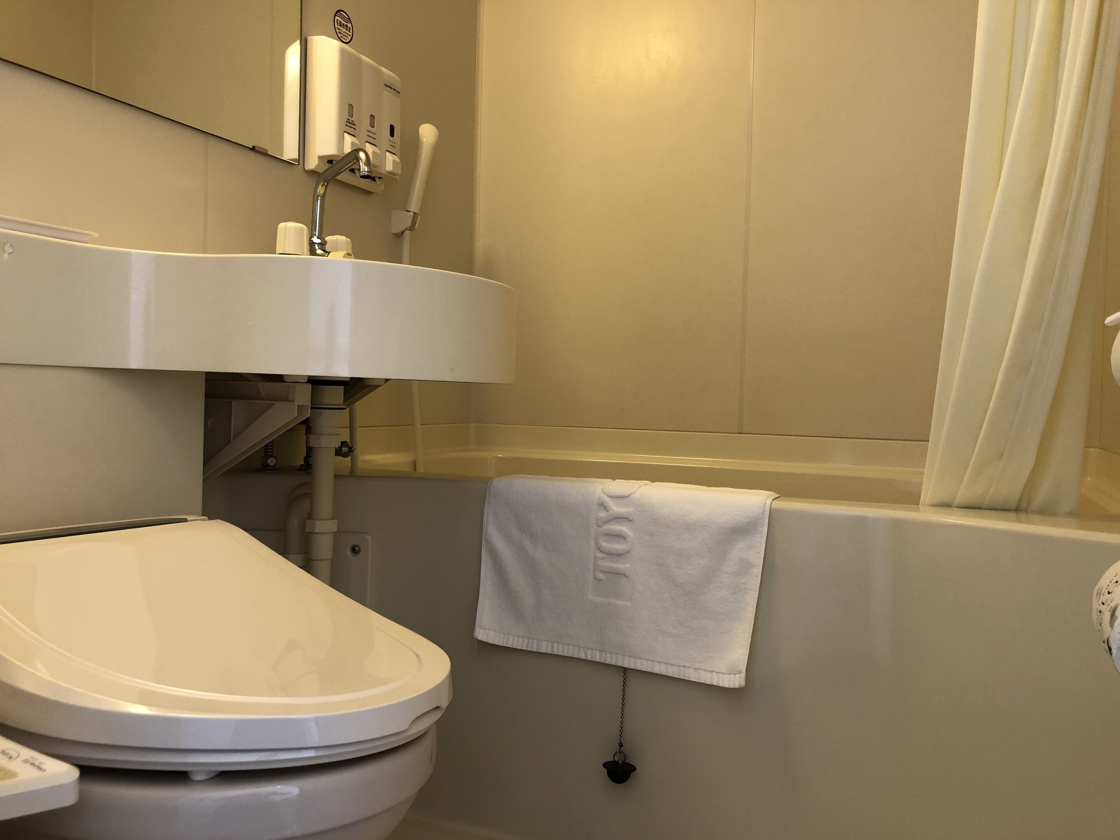 Een bad/douchecombinatie, pantoffels, toiletten met elektronisch bidet
