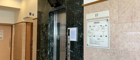 An elevator with a digital display, a coin laundry sign, and an emergency exit map on the wall.