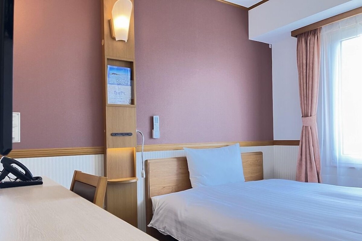 A hotel room with a bed, a desk, a telephone, and a wall-mounted shelf with a lamp.