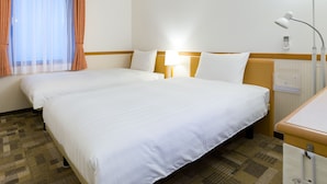 A hotel room with two single beds, a bedside table with a lamp, a window with sheer curtains, and a wall-mounted control panel. - Toyoko Inn Shonan Hiratsuka Station Kita 1 (Hiratsuka)