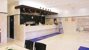 A hotel reception area with a marble counter, a 'FRONT' sign above it, and a blue carpet with the hotel's logo. - Toyoko Inn Tokyo Fussa Station Higashi (Fussa)