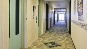 A hotel corridor with multiple doors, a patterned carpet, and ceiling lights. - Toyoko Inn Tokyo Fussa Station Higashi (Fussa)