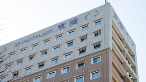 A multi-story building with a modern architectural design, featuring a series of rectangular windows and a prominent sign with blue lettering. - Toyoko Inn Tokyo Fussa Station Higashi (Fussa)