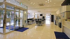 A hotel lobby with a glass entrance, a reception desk, and a seating area with tables and chairs. - Toyoko Inn Tokyo Fussa Station Higashi (Fussa)