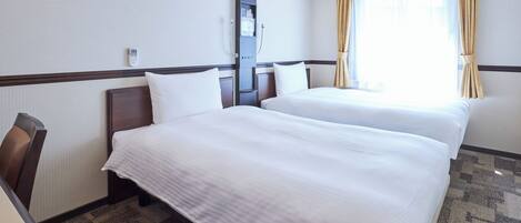 A hotel room with two beds, a desk, and a window with curtains.