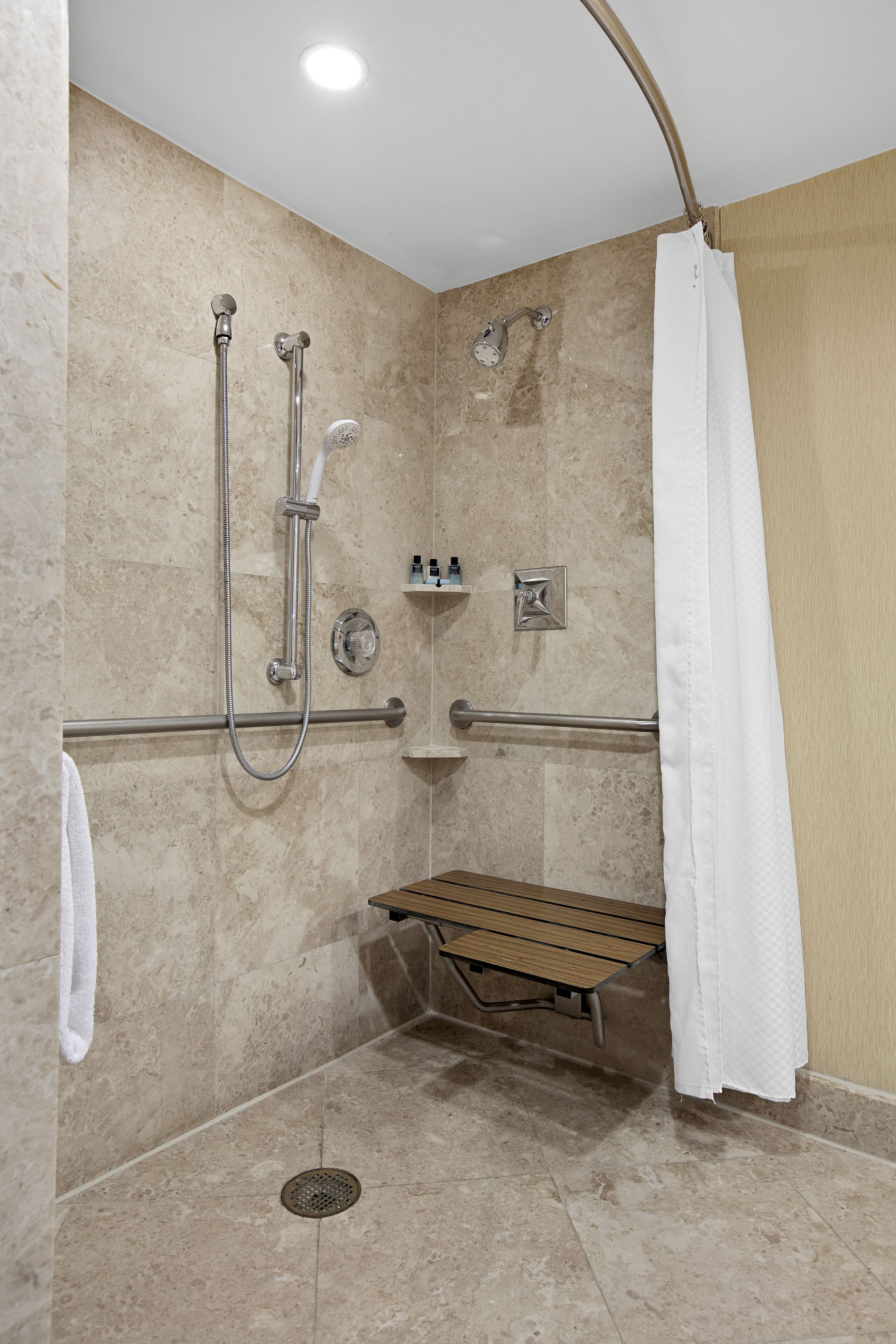 Un espace douche équipé d’un banc, de barres d’appui et d’un sèche-mains.