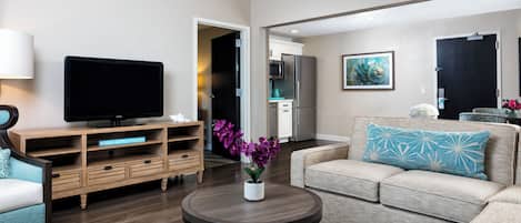 A modern living room with a flat-screen TV, wooden entertainment unit, and a sofa with patterned cushions.