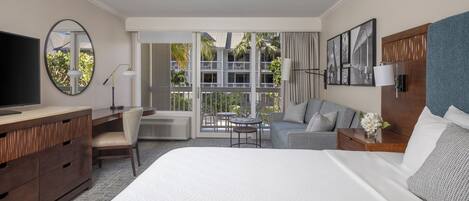 A hotel room with a large bed, a desk, a chair, a TV, a balcony with a view of palm trees, and a dining area.