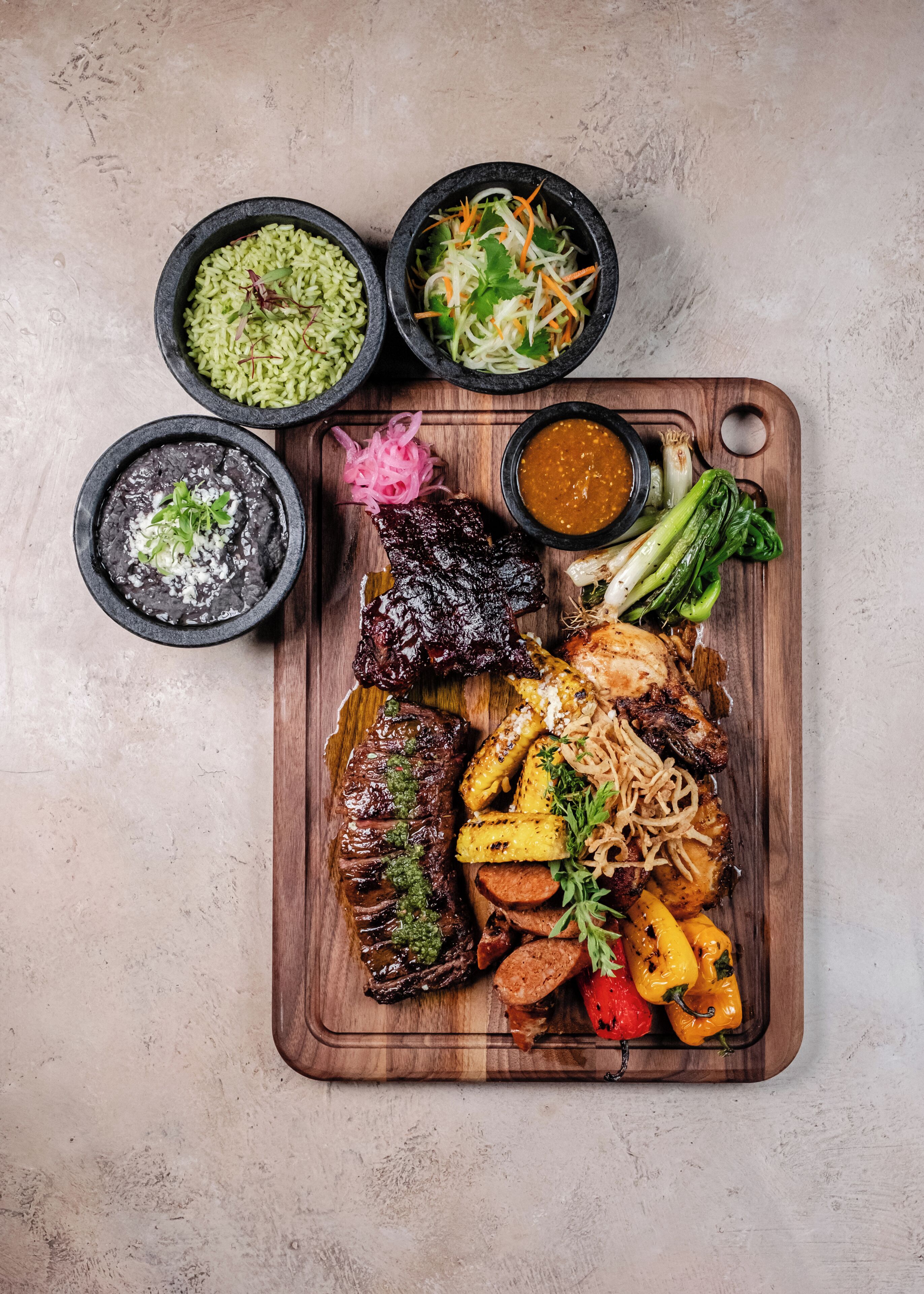 Ein Holzboden mit verschiedenen Gerichten, darunter gegrilltes Fleisch, Gemüse und Soßen.