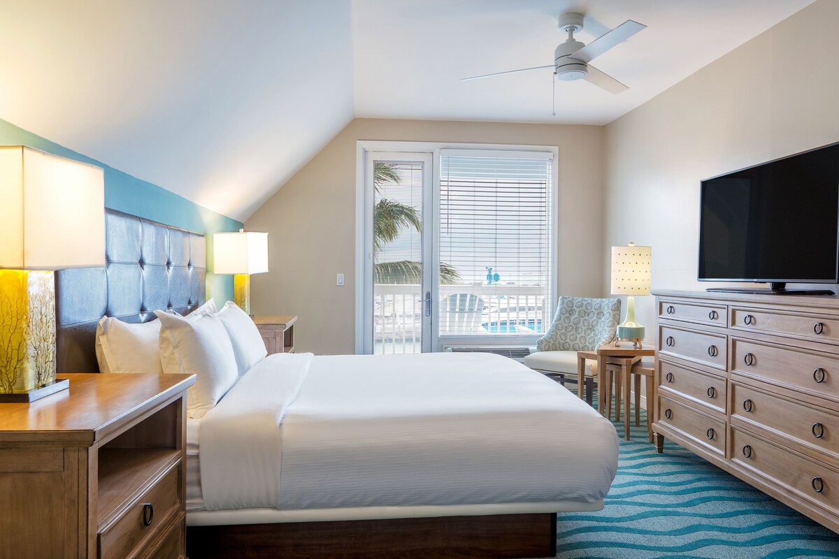 Une chambre d’hôtel avec un grand lit, une télévision, une commode et un ventilateur de plafond.