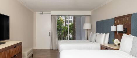 A hotel room with two beds, a TV, a wooden dresser, a nightstand with a lamp, and a view of palm trees through the window.