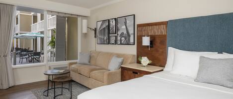 A hotel room with a bed, a sofa, a small table, and a view of the outdoor area.
