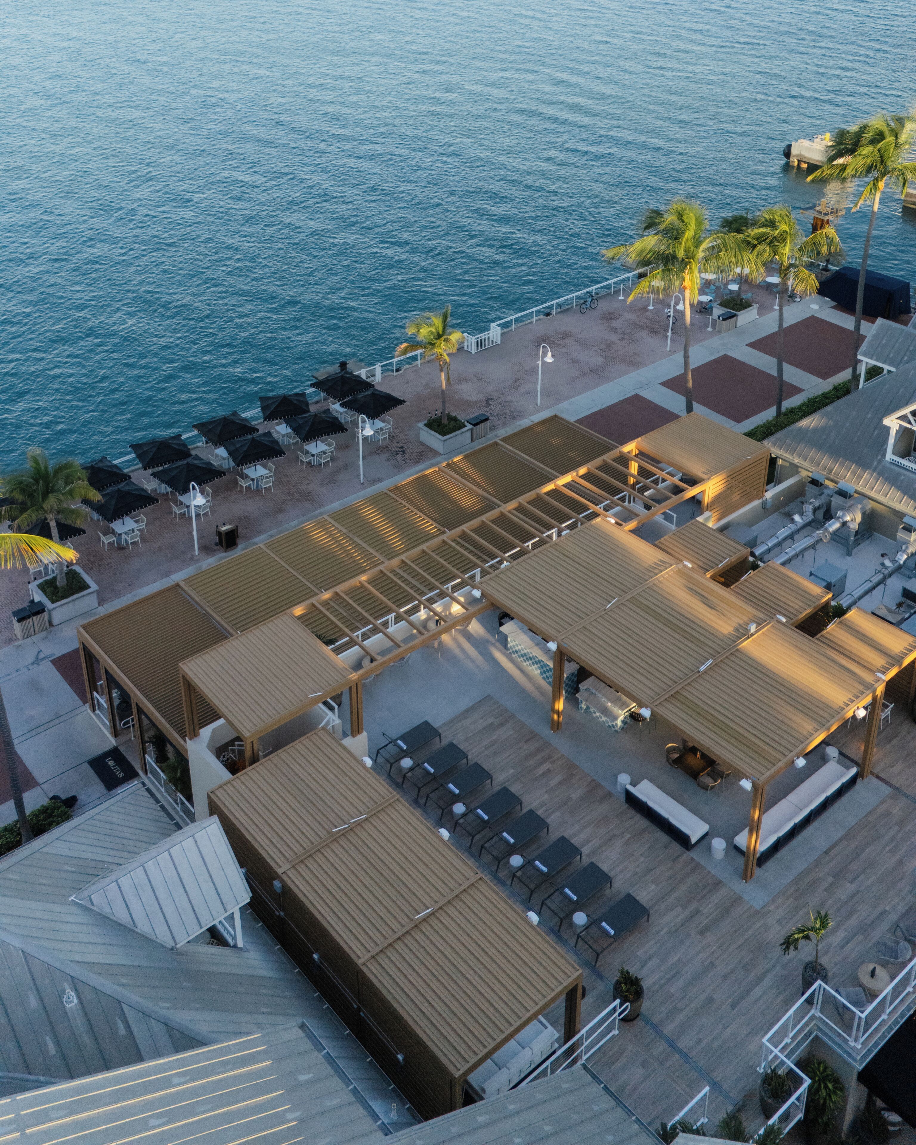 An aerial view of a resort with outdoor seating areas, a pool, and a beach.