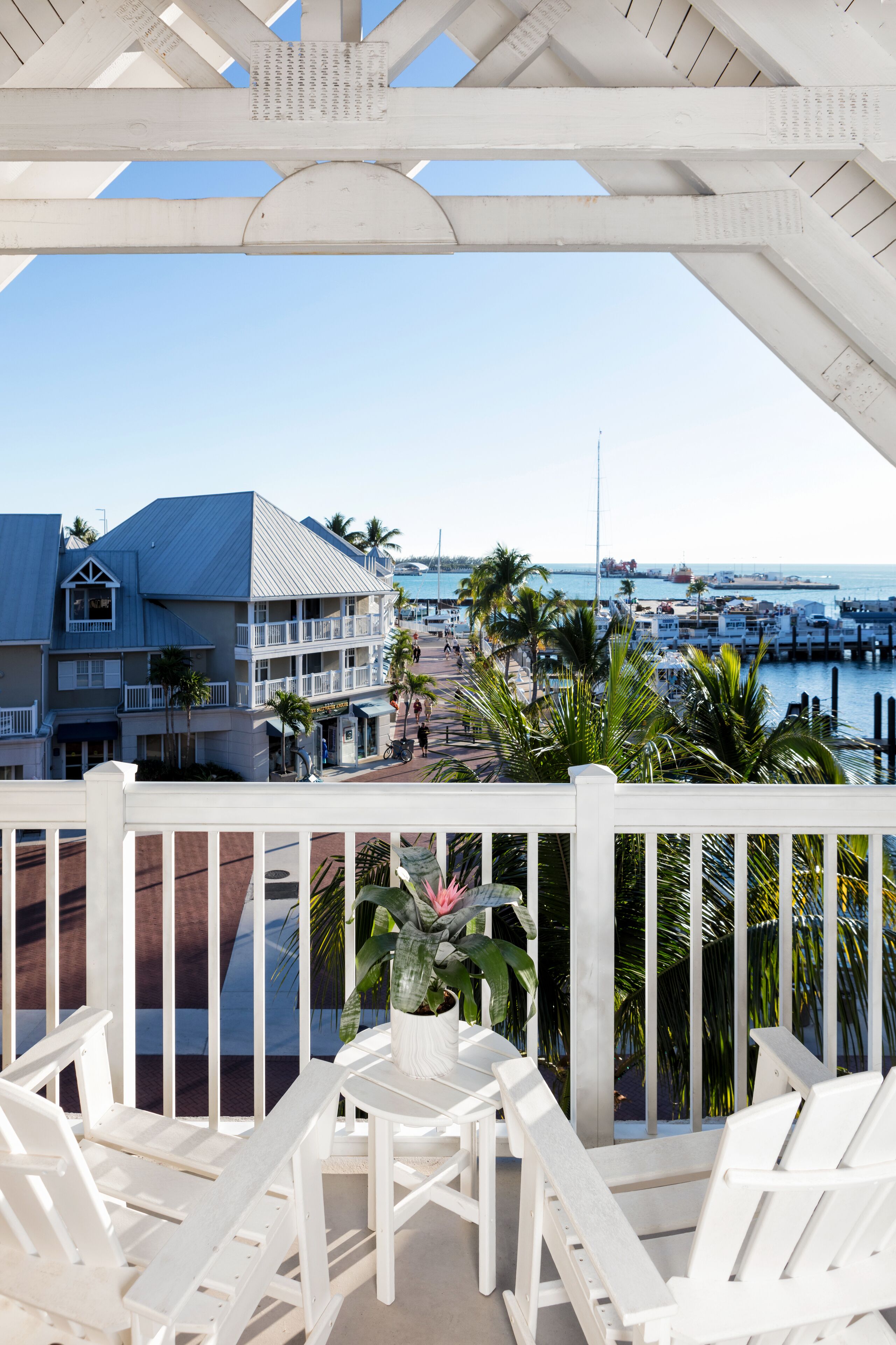 Un balcon avec des balustrades blanches, des chaises blanches et une vue sur une marina avec des bateaux et des bâtiments.