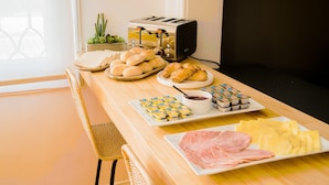 A breakfast buffet with bread, pastries, ham, cheese, and condiments on a wooden table. - Casa Baquedano (Santiago)