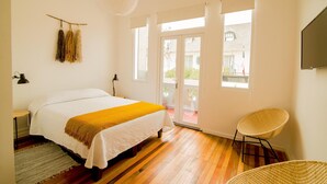 A bedroom with a bed, two bedside lamps, a hanging plant, a window with a view, and a wicker chair. - Casa Baquedano (Santiago)