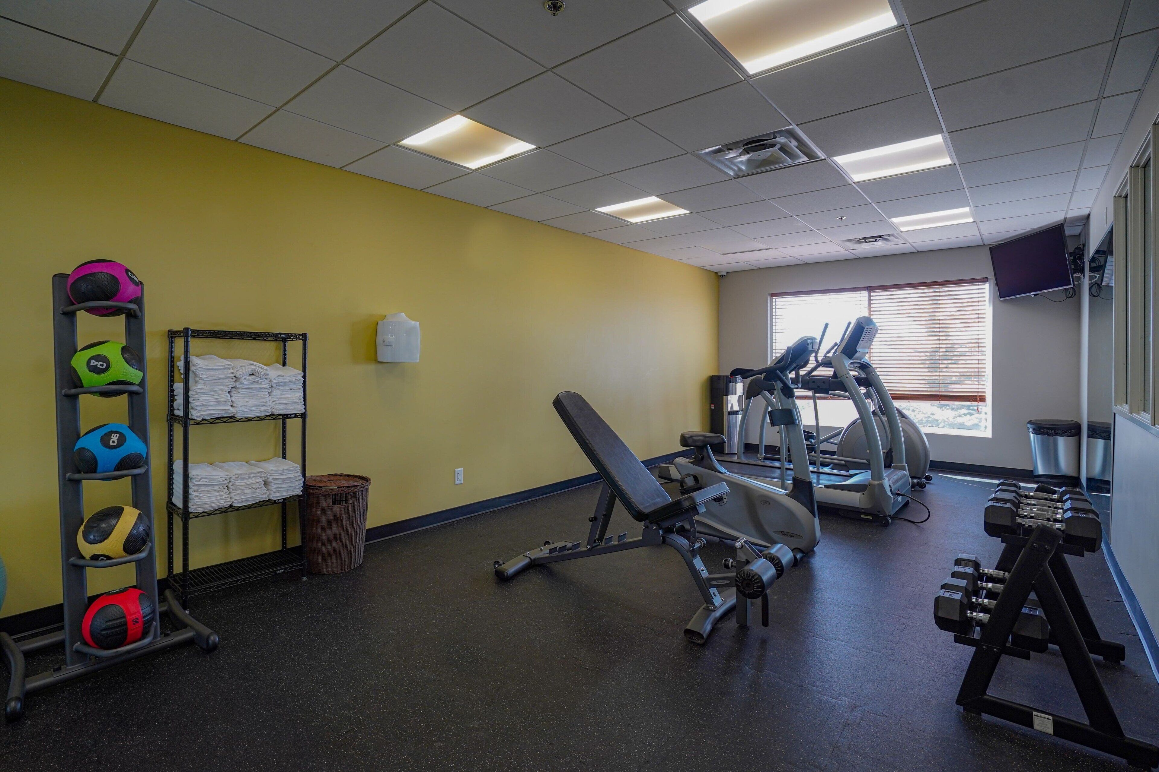 A gym with exercise equipment, a wall-mounted TV, and a window with blinds.