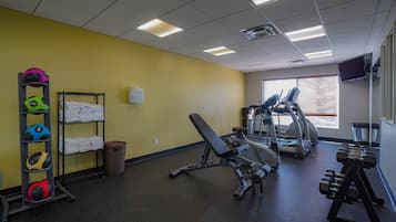 A gym with exercise equipment, a wall-mounted TV, and a window with blinds.